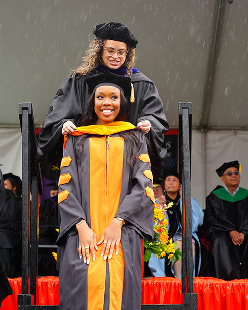 Psychology Professor Aileen Torres places the doctoral hood upon PsyD graduate Amanosi Agbugui.