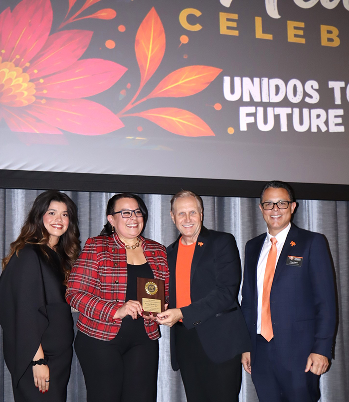 Maribel Rodriguez receives a commemorative plaque from President Richard J. Helldobler, joined by Kim Galvez and Roy Garcia